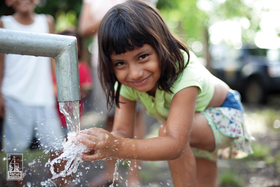 young girl holding hands under water flowing from pipe